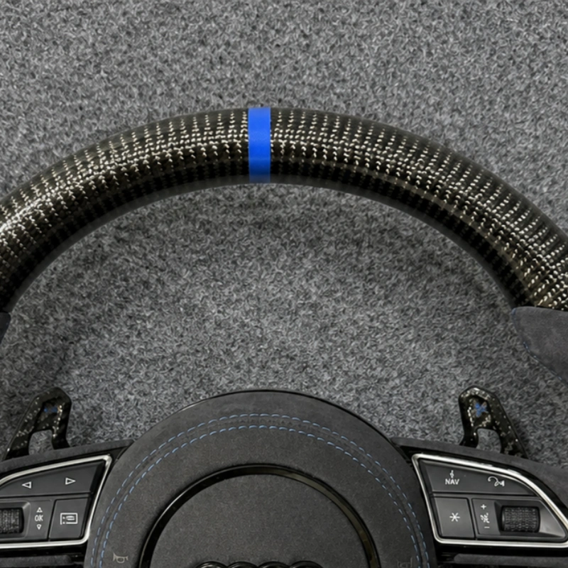 Close-up of bright blue 12 o'clock center mark and glossy carbon fiber texture on Audi S6 steering wheel