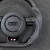 Metal S sport emblem at bottom of Audi flat bottom carbon fiber steering wheel, closeup detail shot