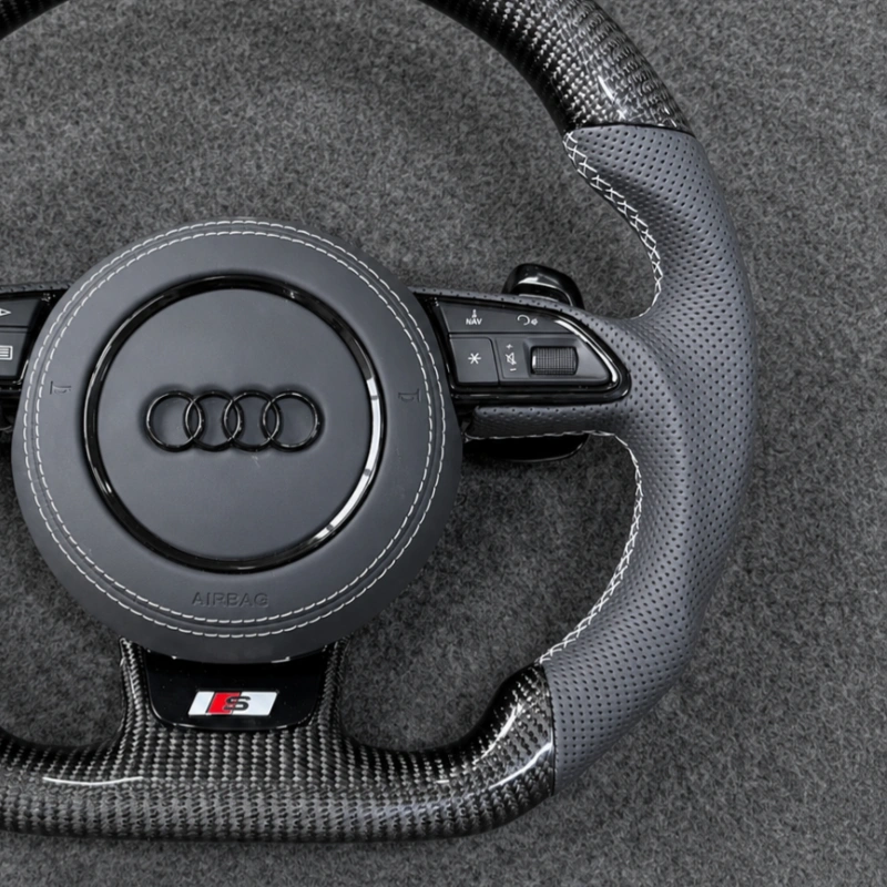 Metal S sport emblem at bottom of Audi flat bottom carbon fiber steering wheel, closeup detail shot