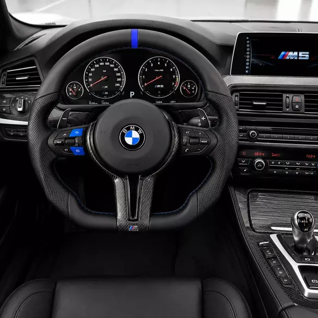 Custom blue accent steering wheel installed in a BMW M5 cockpit with perforated leather and carbon fiber trim