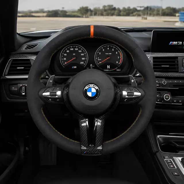 Custom BMW M3 Alcantara and carbon fiber steering wheel with orange center stripe installed in the cockpit