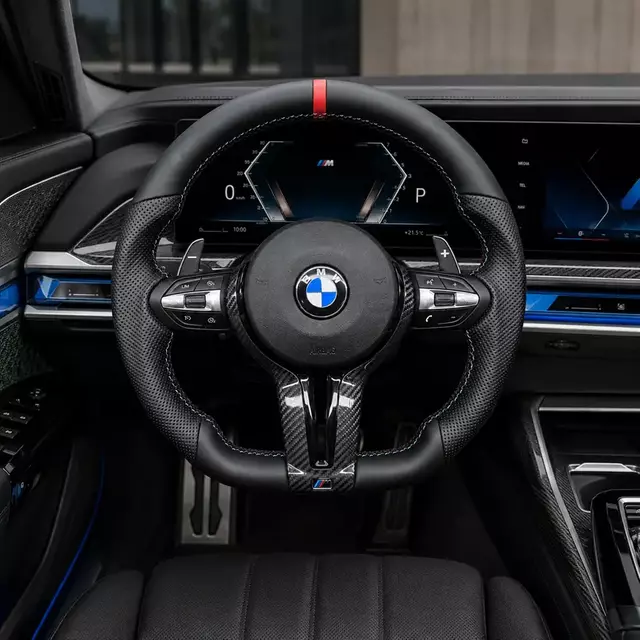 Carbon fiber flat-bottom steering wheel installed in a BMW M7-style cockpit with perforated leather and paddle shifters